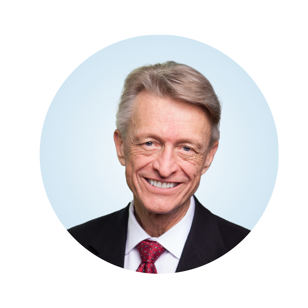 Head-and-shoulders portrait of a smiling older man with light gray hair, wearing a dark suit, white shirt, and red tie, against a light blue circular background.