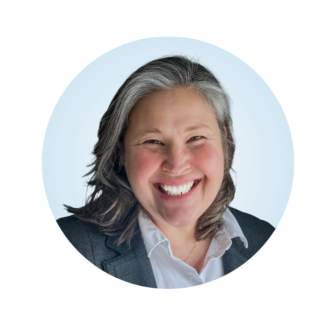 Smiling caucasian female, wearing a gray jacket with a white buttoned shirt centered in a light blue circle.