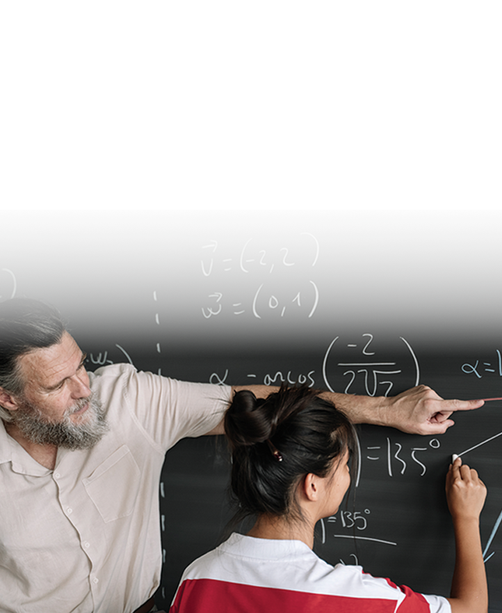 Teacher guiding a student at a chalkboard, pointing to a math equation while the student writes and solves a problem.